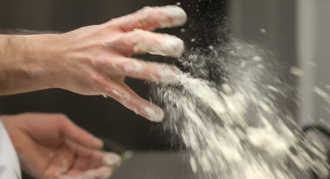 A hand throwing flour to make our PITTABUNS bread